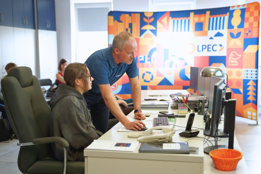 Pracownik LPEC prowadzi zajęcia edukacyjne, pokazując uczennicy pracę z komputerowym systemem monitorowania sieci ciepłowniczej.